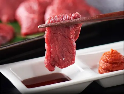 箸で掴んだ馬刺しをタレにつけようとしている写真